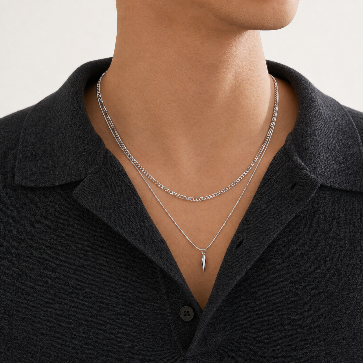 Close editorial view of layered silver curb and spike pendant necklaces