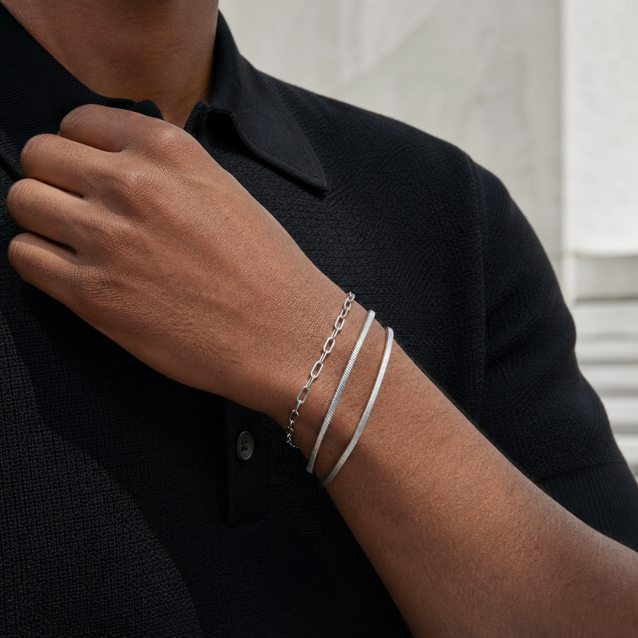 Three layered silver bracelets styled with a black knit polo
